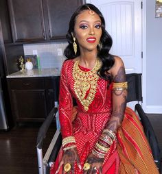 a woman sitting in a chair wearing a red and gold outfit with jewelry on her head