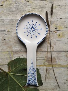 a blue and white spoon sitting on top of a wooden table next to a leaf