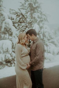 a man and woman standing next to each other in front of snow covered trees