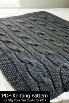 a gray knitted blanket sitting on top of a bed