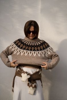 a woman wearing a sweater and scarf with her hands on her hips