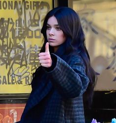 a woman giving the thumbs up sign while standing in front of a storefront window