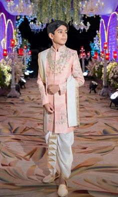 a young man in a pink outfit standing on a runway with chandeliers hanging from the ceiling