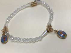 This is an adjustable elastic white/transparent beaded bracelet with three color Divine Child Jesus (Divino Niño in spanish) charms. The bracelet also includes gold colored details. The Divine Child Jesus, also known as Divino Niño or Divino Niño de Bogotá, is a 20th-century religious statue of the child Jesus originating from Bogota, Colombia. It is claimed to have miraculous powers of fertility and healing. The statue is a reminder of God’s tender love for humanity and the openness God has for each one of us. His arms are reaching out to us, just like any child who wants to be picked up. He invites us to take him up into our own arms, pressing him close to our heart. Diameter: 2.75 in. In pictures, size of charms can be compared to a quarter of a dollar. Miraculous Powers, Love For Humanity, White Beaded Bracelet, White Beads Bracelet, Child Jesus, White Beads, Three Color, Bracelets And Charms, In Spanish