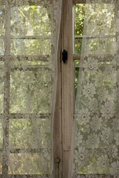 an open window with sheer curtains and flowers on it