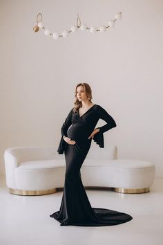 a pregnant woman standing in front of a white couch wearing a black gown with long sleeves