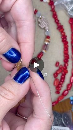 two hands with blue and red nail polish on their fingers, one is holding a beaded necklace