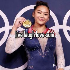 a woman holding up a gold medal in front of a blue wall with the words live laugh love suni