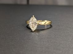 a yellow gold ring with a pear shaped diamond in the center on a black surface