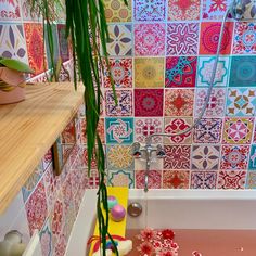 a bathtub with colorful tiles on the wall and floor next to a potted plant