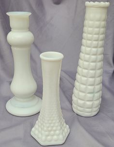 three white vases sitting next to each other on a purple cloth covered surface,