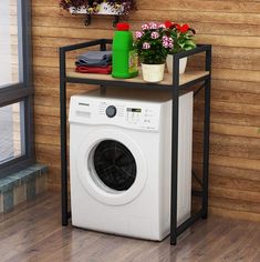 a washing machine sitting on top of a wooden floor next to a shelf filled with flowers