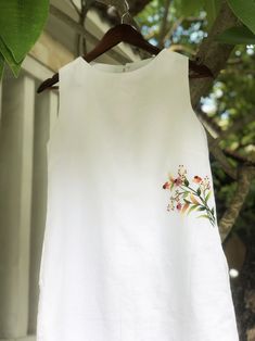 a white shirt with flowers on it hanging from a tree