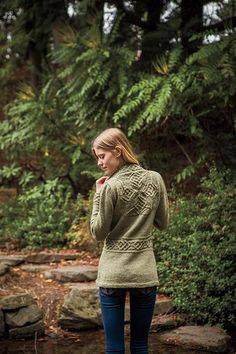 a woman standing in front of some trees and rocks with her hand on her face