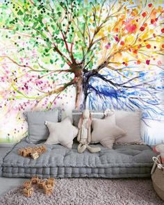 a living room filled with furniture and a large tree mural on the wall behind it