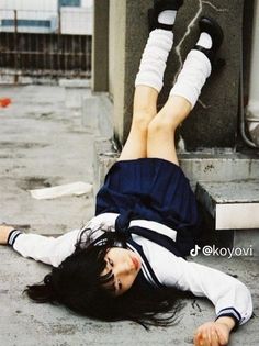 a woman laying on the ground with her feet up in the air next to a building