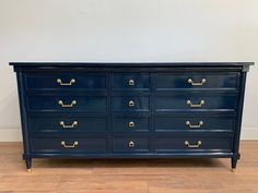 a blue dresser with gold handles on it's sides and drawers, in front of a white wall