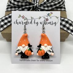 a pair of earrings with an orange and black gnome on it sitting in front of a card