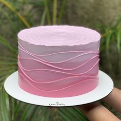 a hand holding a cake with pink icing