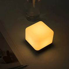 a square light sitting on top of a table next to a knife and glass vase