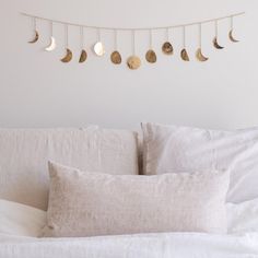 a white bed topped with lots of pillows next to a string of gold moon phases