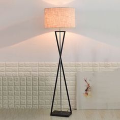 a floor lamp with a white shade on it in front of a wallpapered background