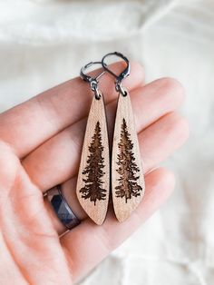 a pair of wooden earrings with pine trees on them are being held in someone's hand