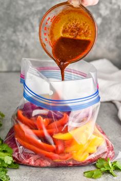 a person pouring dressing into a bag filled with sliced peppers and carrots on top of a counter