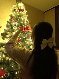 a woman standing in front of a christmas tree with her hand on the top of it