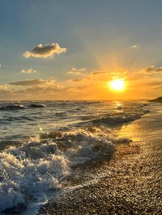 the sun is setting over the ocean with waves crashing on the shore and sand in front of it