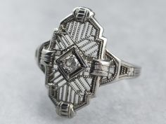 This ring has all the details of lacy Art Deco filigree: intricate crisscrossing of swirling lines, floral motifs, and contrasting geometric designs. Constructed of 18 karat white gold, the center of this ring features a lovely round diamond, in beautiful square mounting which makes the diamond appear larger and square. Classic Art Deco elegance! Metal: 18K White Gold Gem: Diamond .04 Carats Gem Measurements: 2.0 mm, Round Ring Size: 5.50 Marks: "18K" Stamped on the inside band 1920’s Rings, Art Deco Rings 1920s, Art Deco Jewelry 1920s, Dinner Ring, Art Deco Filigree, Edwardian Ring, Rings Ideas, 1920s Vintage, Art Deco Diamond Rings