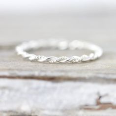 a white gold wedding band with twisted leaves on it, sitting on top of a piece of wood