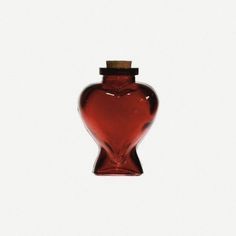 a red glass vase with a wooden top on a white surface, in the shape of a heart