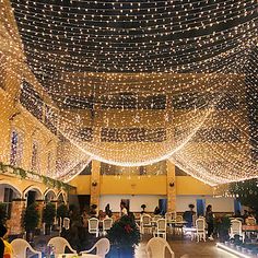 the inside of a building with tables and chairs covered in fairy lights on the ceiling