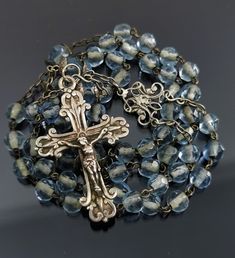 A beautiful vintage French blue rosary with silver crucifix cross, in good condition. Rosary measures approx. 39 cm (15 inch) in length and has nice transparent blue glass faceted beads which are intact and very pretty. The connector is ornate, this interesting rosary would make a nice gift for someone special or a collector. Box on photos is NOT included! A stunning religious jewelry shop well worth a visit ... https://www.etsy.com/shop/100saints. PLEASE LOOK AT THE PICTURES, THEY ARE PART OF T Blue Crucifix Necklace For Spiritual Purposes, Blue Crucifix Necklace For Spiritual Wear, Blue Cross Rosary As Gift, Blue Gemstone Beads Rosary For Spiritual Use, Handmade Blue Rosary With Cross, Handmade Blue Rosary With Cross Shape, Blue Rosary With Round Beads For Gift, Vintage Silver Rosary With Round Beads, Blue Rosary With 8mm Beads In Cross Shape