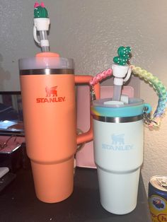 two travel mugs sitting next to each other on a table with an orange cup in the middle