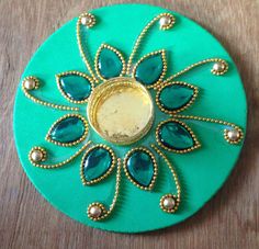 a green circular object with gold accents and blue stones on it's side, sitting on a wooden surface