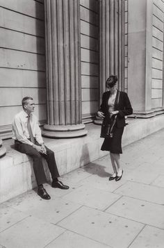 a man and woman sitting on the side of a building next to pillars with columns