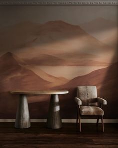 two chairs and a table in front of a wall with a mountain scene on it