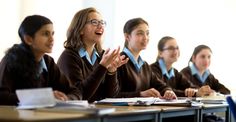 a group of young women sitting at desks in front of each other with their hands together