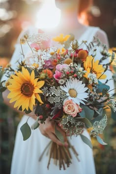 a bride holding a bouquet of sunflowers and greenery in her hands with the sun shining behind her