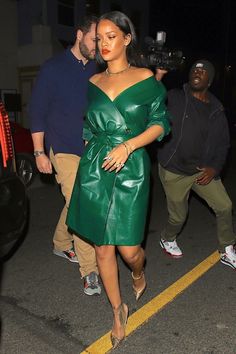 a woman in a green leather dress walking down the street with a man behind her