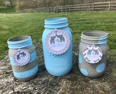 three blue mason jars sitting on top of a tree stump in the grass next to a fence