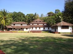 a large white building sitting in the middle of a lush green field next to trees