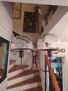 a chandelier hanging from the ceiling in a room with wooden stairs and pictures on the wall