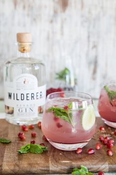 two glasses filled with pomegranate and garnished with mint on a wooden cutting board