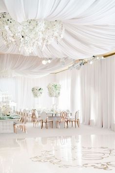 an elegant wedding reception with white draping and floral centerpieces on the ceiling