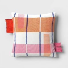 an orange, pink and white plaid pillow with tassels on the edge is shown