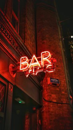 a neon sign that reads bar at night on the side of a red brick building