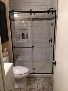 a white toilet sitting next to a shower in a bathroom on top of a hard wood floor